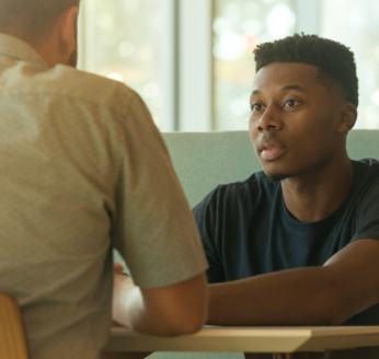 Two people talking over a desk near a window